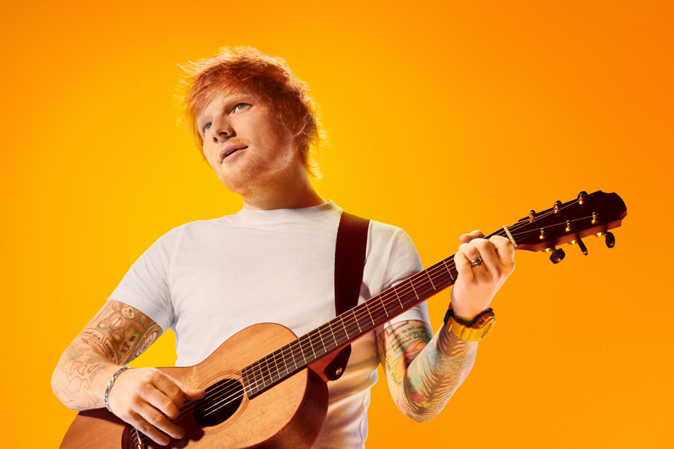 Singer-songwriter Ed Sheeran is shown playing his guitar against an orange background.