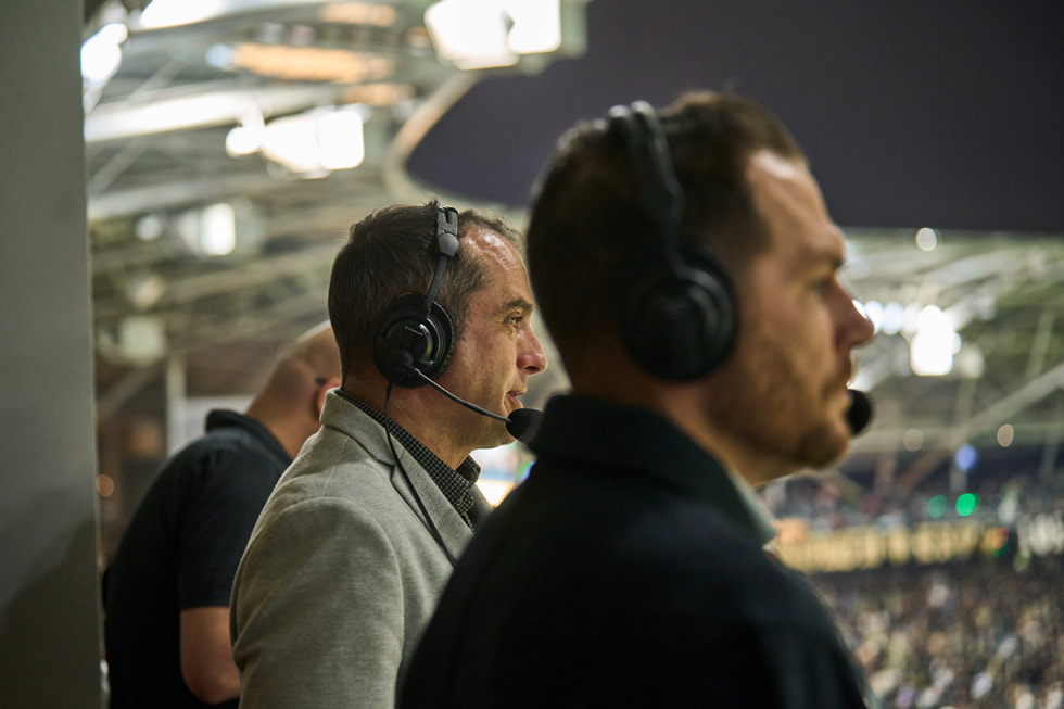 Broadcasters Max Bretos and Brian Dunseth are shown wearing headsets behind the scenes at an LAFC match.