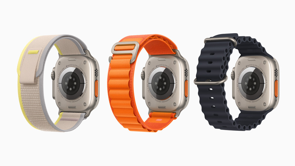 Três aparelhos Apple Watch Ultra são mostrados pela parte de trás para exibir as três diferentes pulseiras, incluindo uma pulseira loop Trail em cinza e amarelo, uma pulseira loop Alpina em laranja e uma pulseira Oceano em preto. 