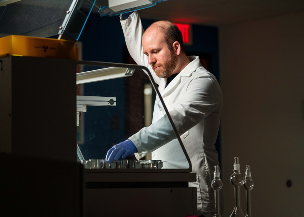 Un homme portant une blouse et des gants travaille avec des machines dans un laboratoire.