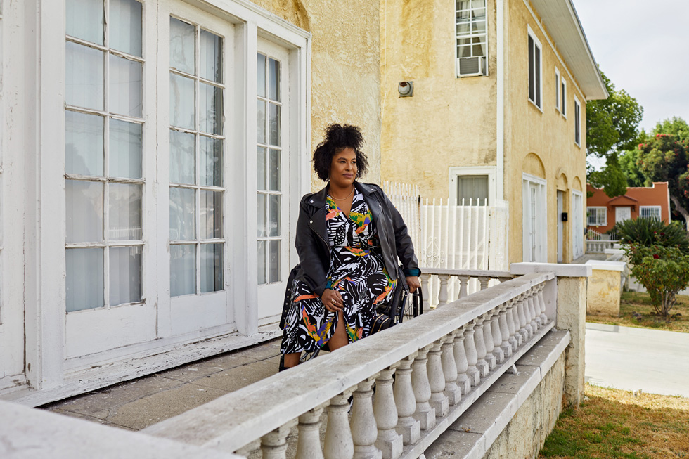 Tatiana Lee, wearing a black leather motorcycle jacket over a boldly patterned dress, sits in her wheelchair outside.