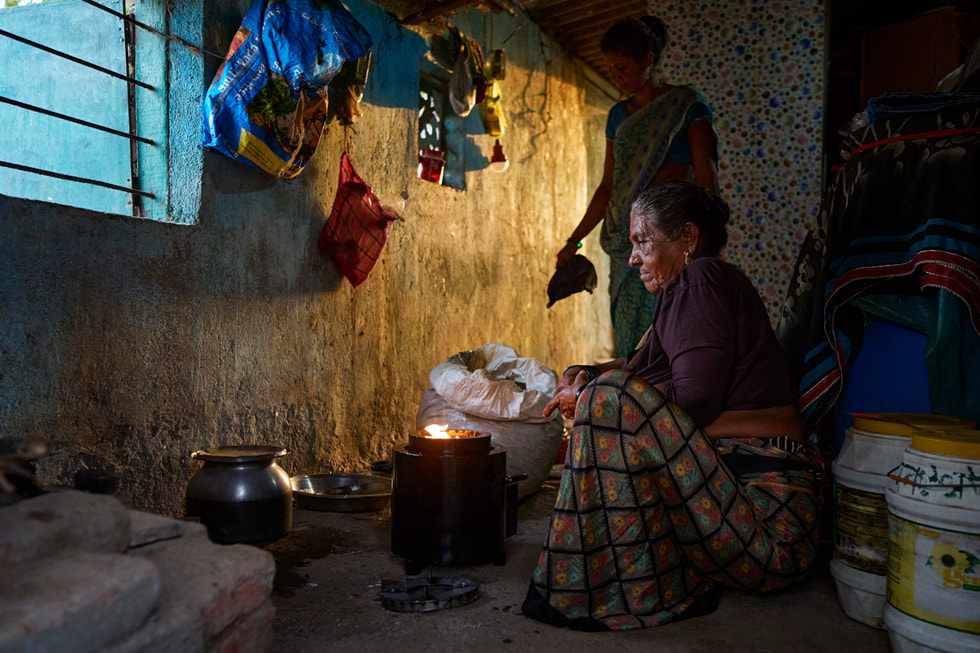 Twee Indiase vrouwen rond een draagbaar bio-kooktoestel op alternatieve brandstof.