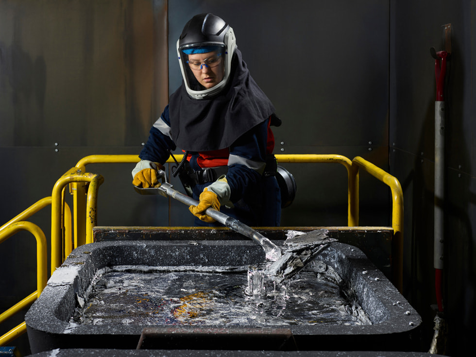 A worker wearing safety equipment smelts aluminum in a factory setting.