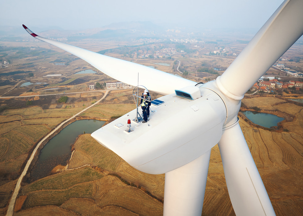 Deux ouvriers se tiennent au sommet d’une immense éolienne située dans un parc éolien de la province de Hubei, en Chine.