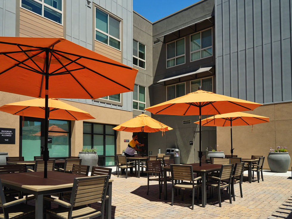 Picnic tables with umbrellas sit outside of the three-story Veterans Square housing complex.
