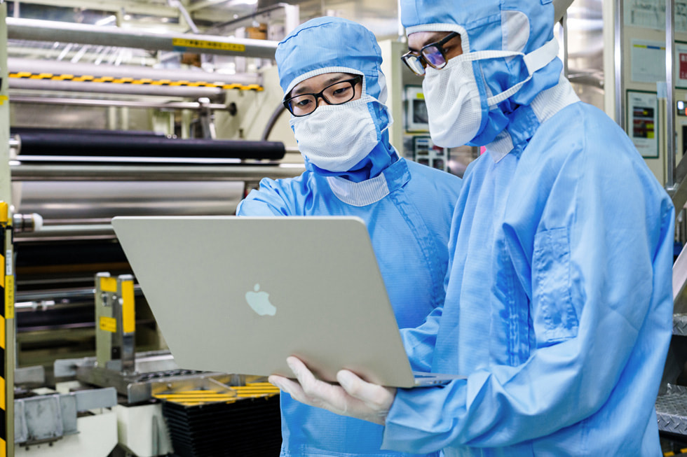 保護具を着た2人の作業員が、ラボでMacBookを検査しているところ。