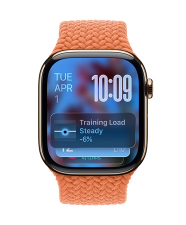 Apple Watch w kolorze różowego złota z plecionym paskiem w kolorze mandarynkowym. W lewym górnym rogu tarczy widać datę, w prawym górnym rogu cyfrowy zegar w orientacji pionowej, a na dole widżet Obciążenia treningowego – wszystko przejrzyste dzięki Liquid Glass.