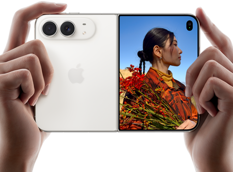 iPhone Duo, culoare Alb stelar, ținut de două mâini în dispunere orizontală, desfășurat, partea din stânga prezintă camerele spate Dual Fusion de 48 MP, partea din dreapta prezintă o persoană care se pozează pe ecranul extern, subiectul pozelor poate vedea chipul său în timp ce poza este făcută cu ajutorul aplicației Previzualizare Duo