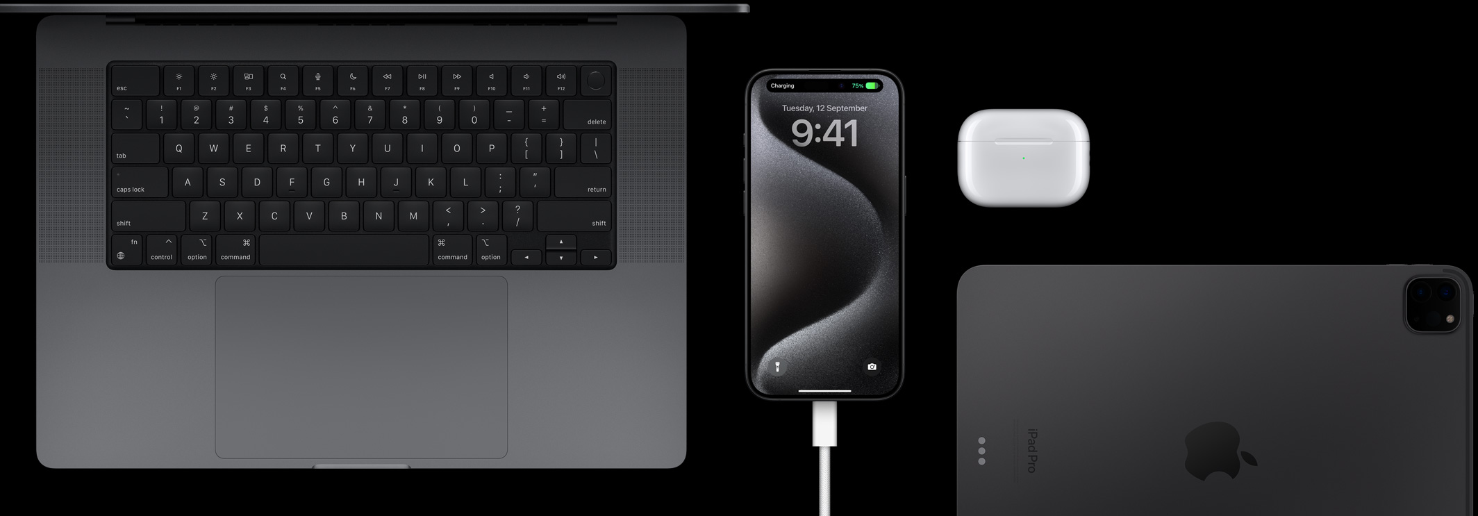 iPhone 15 Pro with a USB-C cord plugged into it surrounded by a Macbook Pro, an AirPods Pro, and an iPad
