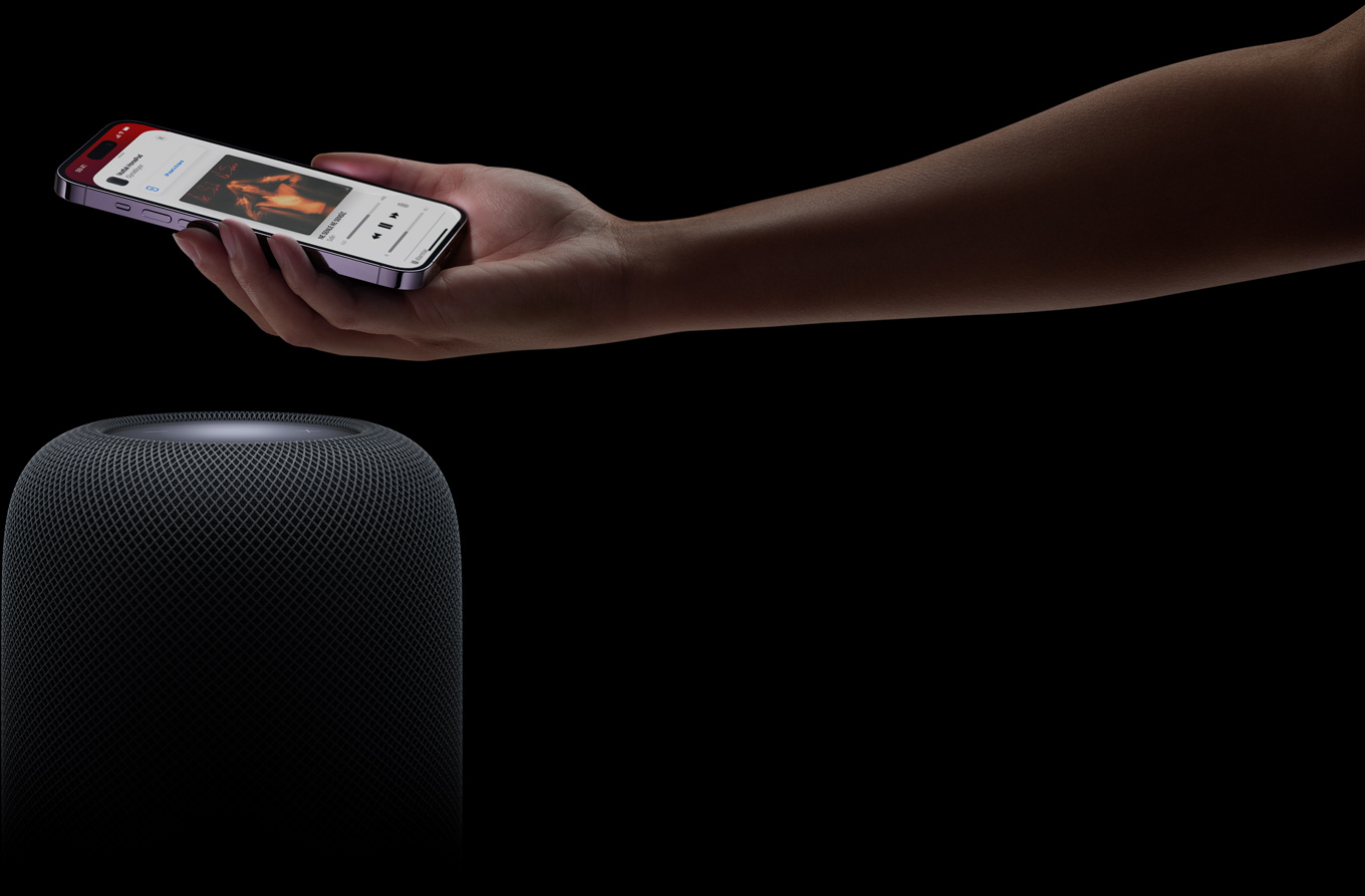 Sayfanın sağ tarafından gelen bir el, bir HomePod hoparlörün üstünde bir iPhone’u tutuyor
