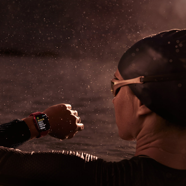 A picture of a swimmer, in a swimming pool, looking at their Apple Watch.