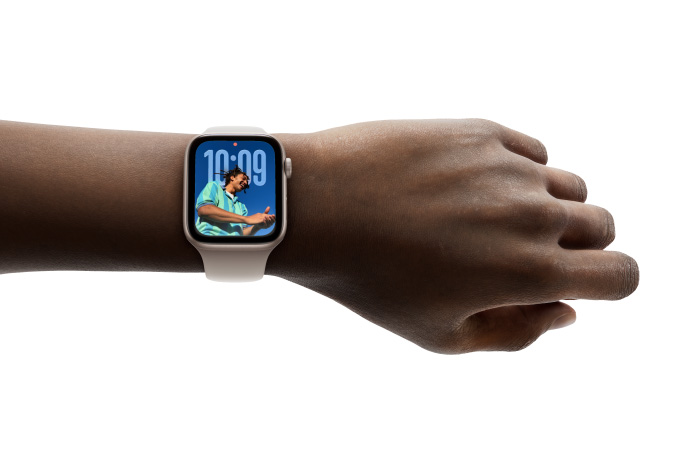 Close-up of Apple Watch in Rose Gold with rubber strap on a person’s wrist, showing Time app in new Liquid Glass design