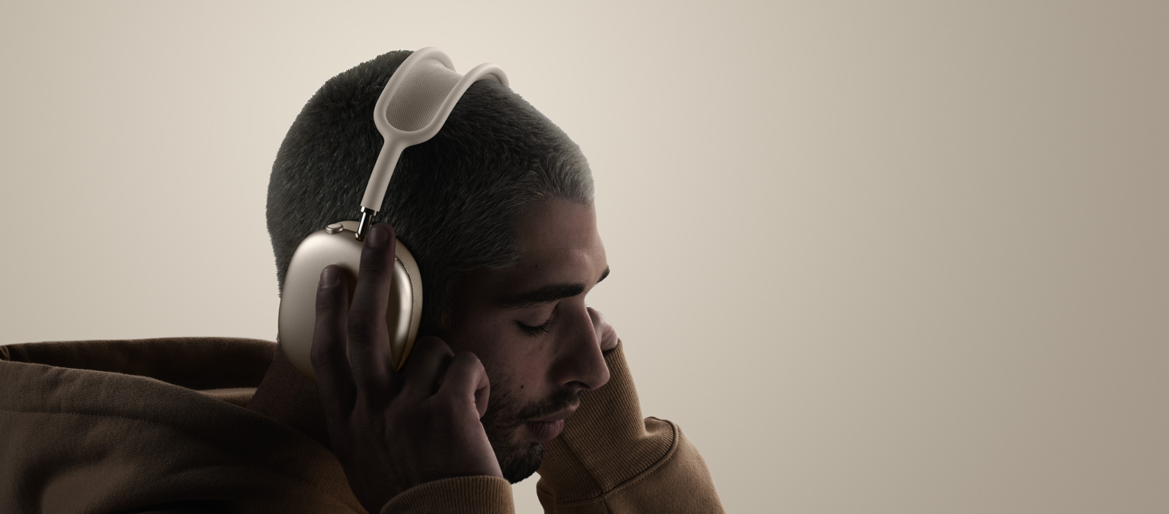 Una persona di profilo che indossa un paio di AirPods Max 2 mostrate di lato e tocca l’esterno dei cuscinetti con le dita