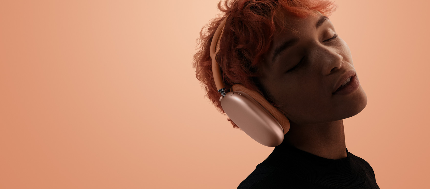 Una persona con la testa reclinata all’indietro e gli occhi chiusi che indossa un paio di AirPods Max 2 arancioni, su uno sfondo arancione-rosa