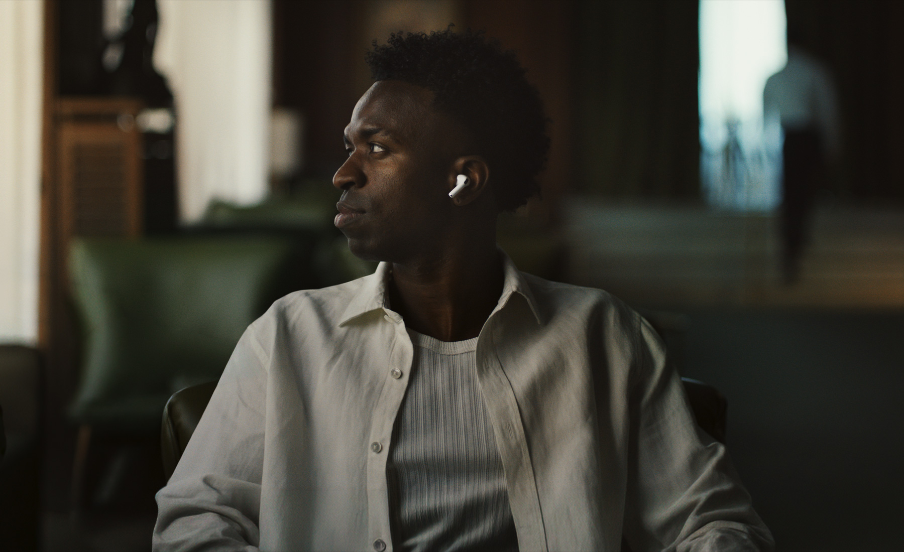 Person wearing white shirt, head turned to the side, left AirPods Pro 3 earbud visible