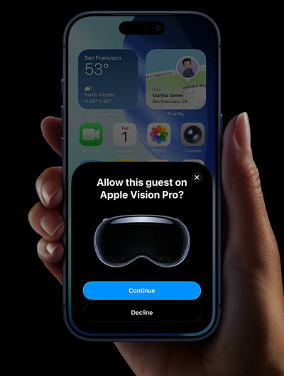 A hand holding an iPhone. The iPhone’s screen displays a window with the message, “Allow this guest on Apple Vision Pro?” with buttons labelled “Continue” and “Decline”.