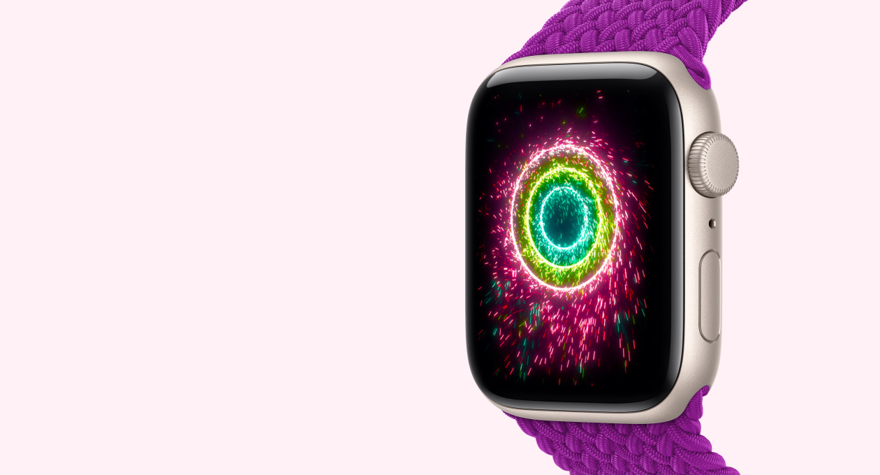 スターライトアルミニウムケースのApple Watch SE 3。マゼンタのブレイデッドソロループバンドが取りつけられている。画面に花火のスタイルのアクティビティリングが表示され、ピンク、ライムグリーン、ライトブルーの同心円状のリングが見える