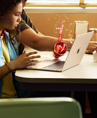 Một người với lấy thứ gì đó trong nhà hàng, làm đổ đồ uống có đá lên chiếc MacBook đang mở