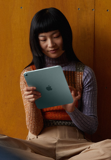 Eine Studentin sitzt auf dem Boden mit dem Rücken an einer Wand. Sie hält ein iPad.