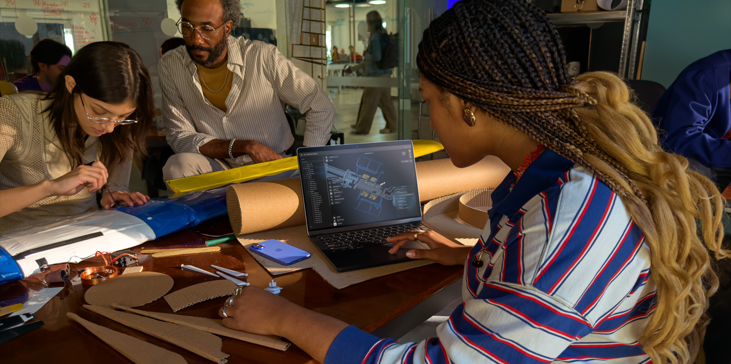Eine Gruppe von Studierenden sitzt an einem Tisch und arbeitet an einem technischen Projekt. Eine Studentin hat ein geöffnetes MacBook mit der Shapr 3D App auf dem Bildschirm vor sich.