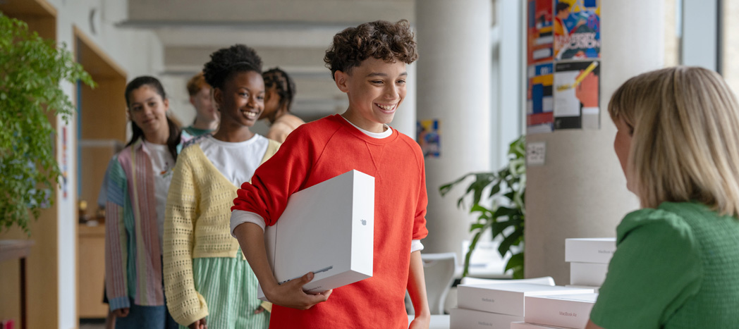 A student receives a MacBook box from the IT team, with other students lined up behind them, highlighting easy deployment