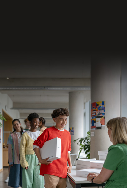 A student receives a MacBook box from the IT team, with other students lined up behind them, highlighting easy deployment