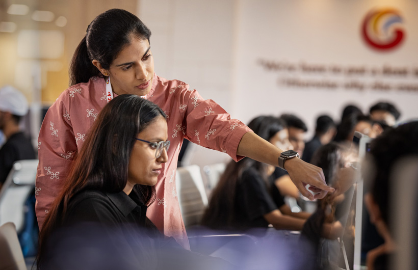 An instructor stands next to her student who’s sitting at her iMac, and points to her screen.