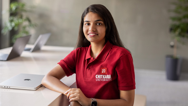 Nishtha Tandon sits at a table with a closed MacBook next to her, smiling at the camera.