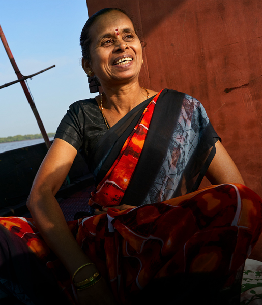 Une femme indienne assise dans un bateau sourit, avec un cours d’eau en arrière-plan