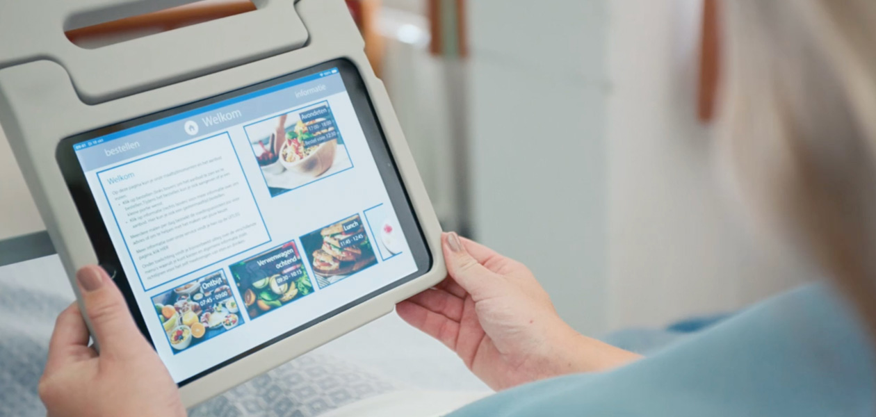 A patient looking at an iPad screen while sitting in her hospital bed.