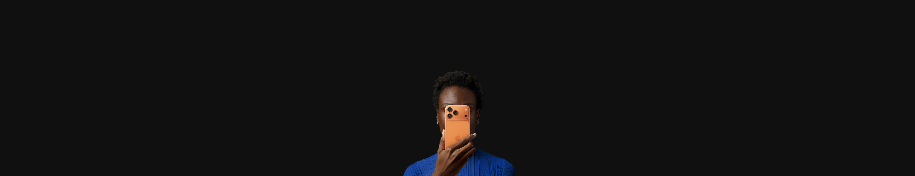 A person holds iPhone 17 Pro in front of their face, back exterior facing outward, Cosmic Orange color.