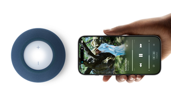 HomePod mini 2 ja iPhone: käsi pitelee iPhonea sinisen HomePod mini 2:n vieressä valmiina siirtämään sisällön laitteelta toiselle
