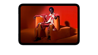 iPad mini displayed, front view, showing a vivid screen with a person in an orange suit, sitting on an orange chair, placed in an orange room.