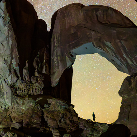 Photograph of a person in a canyon and a star filled night