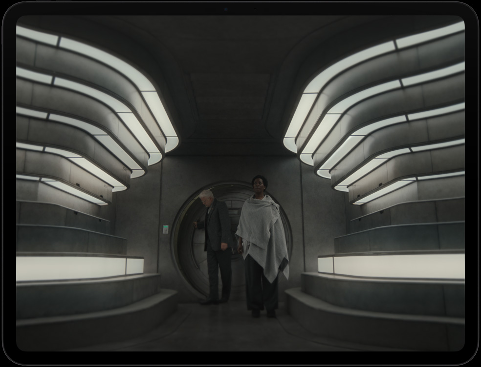 iPad Pro, face avant, orientation paysage, noir sidéral, cadre d’écran noir, écran affichant un vaisseau spatial futuriste avec des machines perfectionnées, une personne en combinaison spatiale interagissant avec des commandes et un équipement