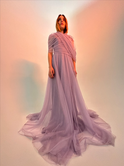 Bilde, kurā redzama sieviete garā ceriņkrāsas kleitā. Bilde uzņemta vājā apgaismojumā ar ultraplatleņķa kameru.