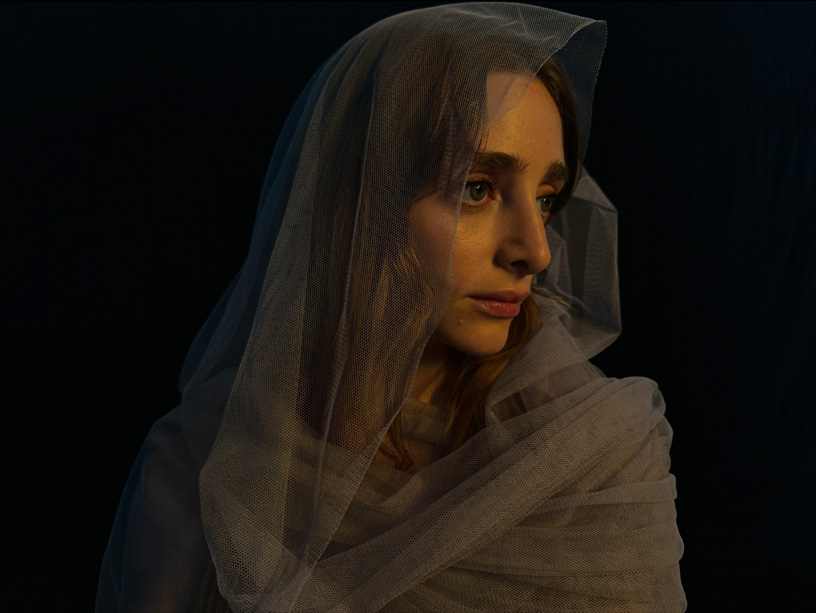 Fotografia de uma mulher envolta num véu, onde se vê com detalhe os fios do tecido.