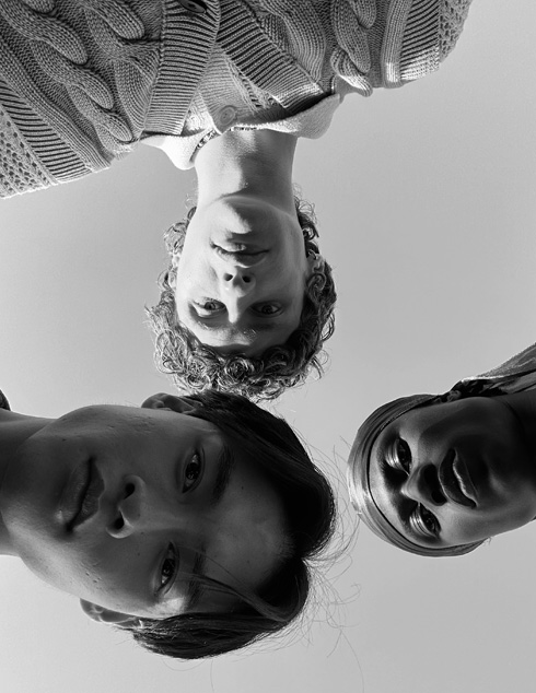 Grupinė asmenukė: trys žmonės stovi skirtingu atstumu nuo fotoaparato. Ši nuotrauka buvo padaryta naudojant „TrueDepth“ kamerą.