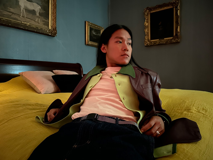 Et farverigt billede af en mand, der ligger på en seng i et svagt oplyst rum, taget med Nat-tilstand.