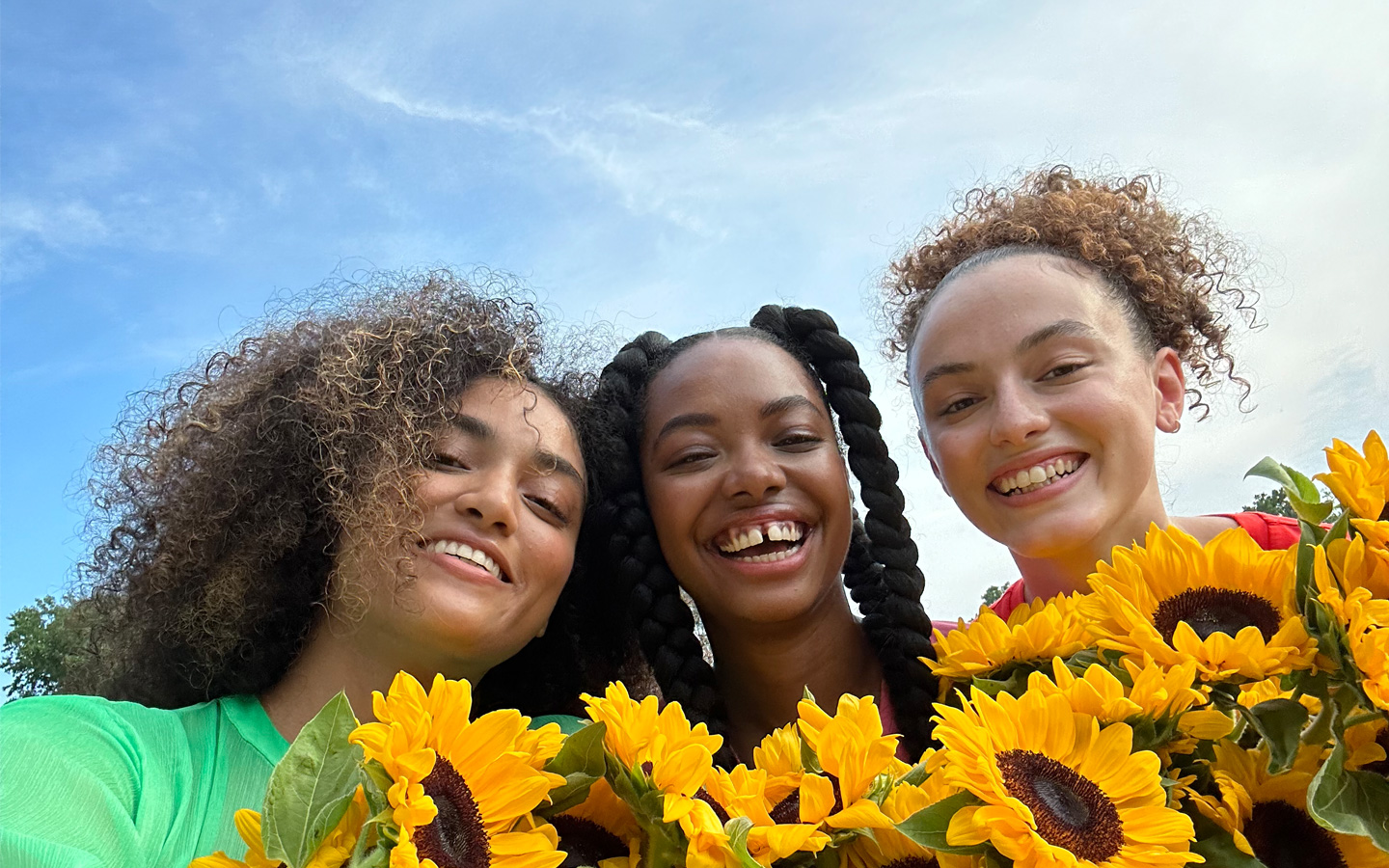 A sharp and vibrant selfie of three people holding yellow flowers, taken with the TrueDepth camera.