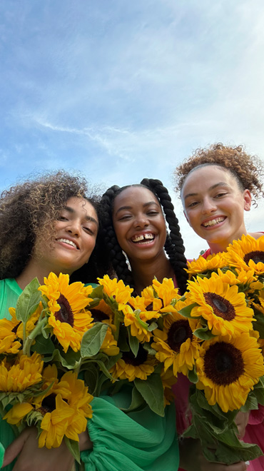 노란색 꽃을 들고 있는 세 사람을 TrueDepth 카메라로 촬영한 선명하고 생생한 색감의 셀피
