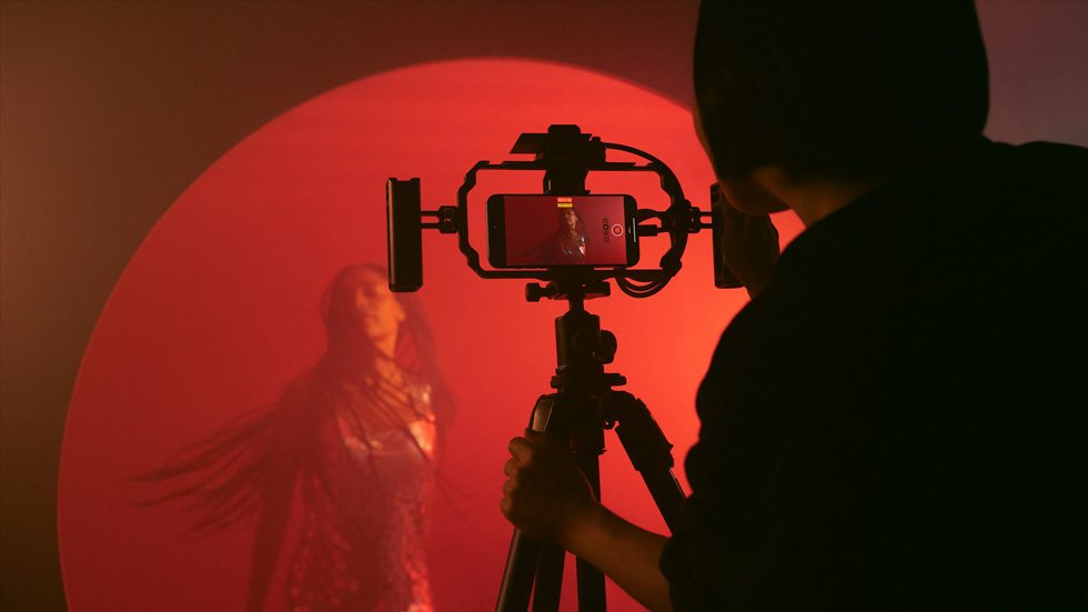 A photo of someone using an iPhone on a tripod to record a colourful video of a woman