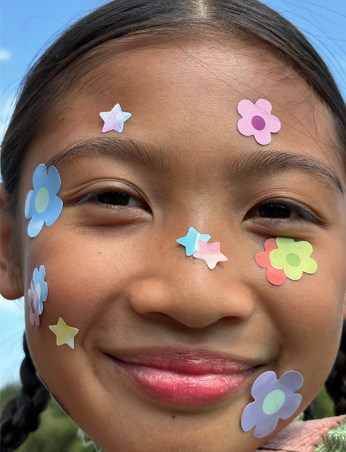 Ultra-Nahaufnahme eines Mädchens mit Blumenaufklebern im Gesicht, aufgenommen mit dem kontinuierlichen Zoom beim iPhone 15