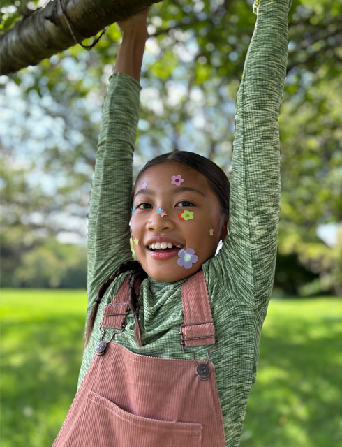 iPhone 15의 광학 줌급 퀄리티의 2배 망원 줌을 사용해 얼굴에 꽃 스티커를 붙인 소녀를 클로즈업하여 촬영한 사진