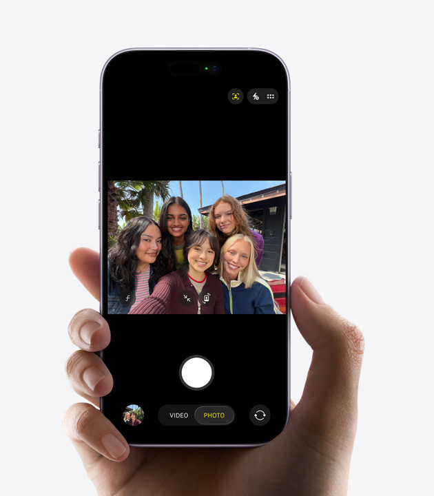 iPhone elölnézetből, a Center Stage előlapi kamera szelfivideót rögzít, az automatikus képkomponálási funkció sárga téglalapkerettel jelöli meg a három szereplő arcát.