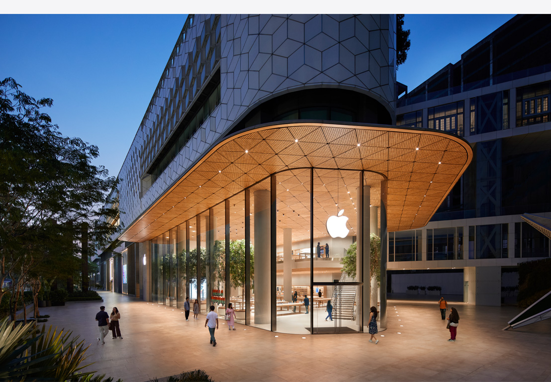 Apple Store üzlet este, üvegablakokkal, bent kivilágítva, a bejárati ajtó felett Apple logóval.