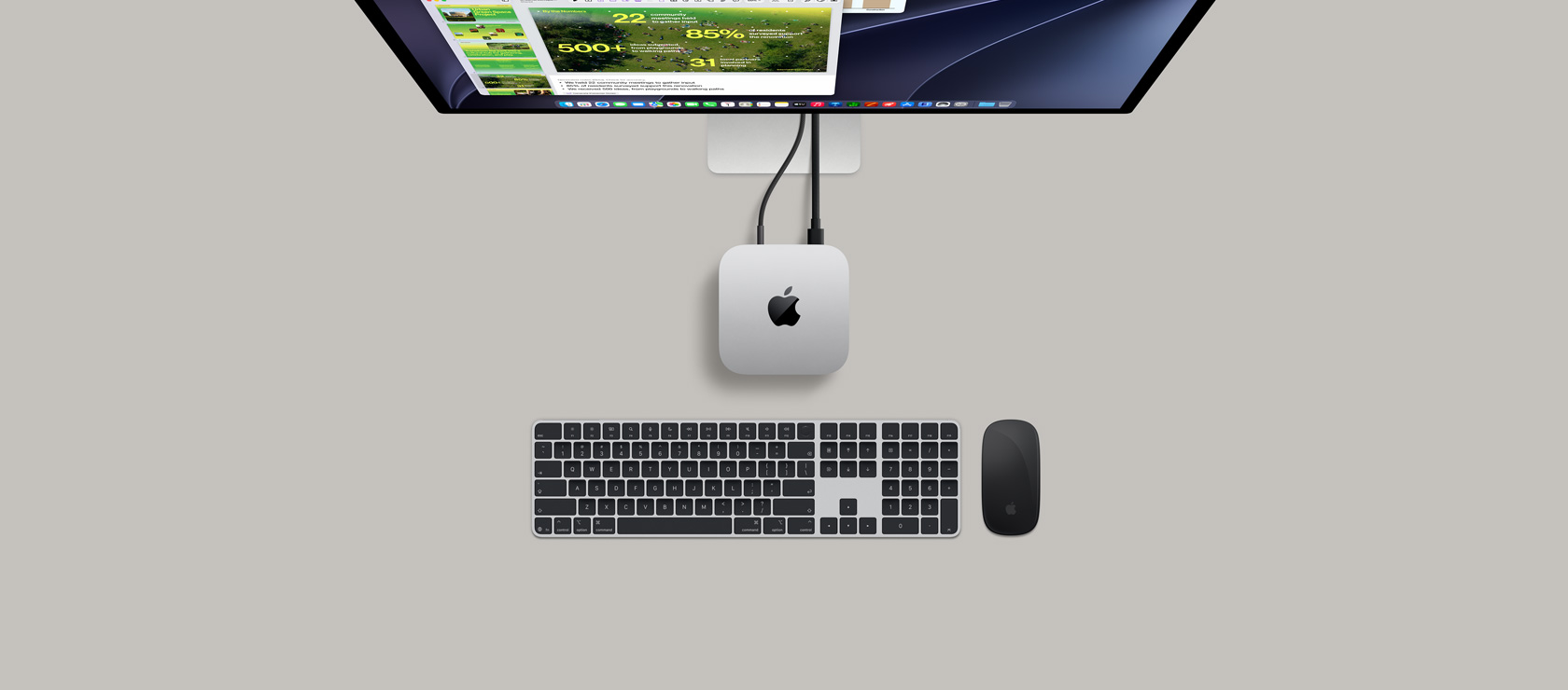 Mac mini, top, silver aluminum, rounded corners, glossy black Apple logo centered, connected by cord, Studio Display partially visible on top with screen showing Calendar app, Keynote presentation, and bar graph open, Magic Keyboard with Numeric Keypad, Magic Mouse visible below Mac mini