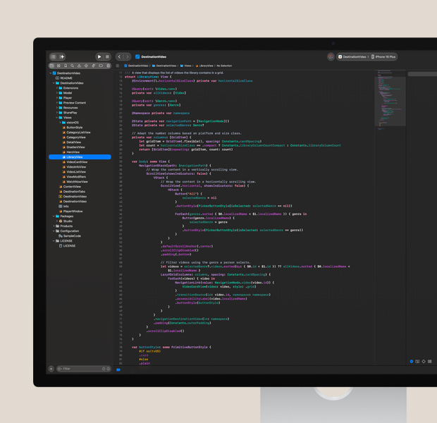 Studio Display screen, Xcode app open with colorful code editor, iPhone with app test partially visible on right side