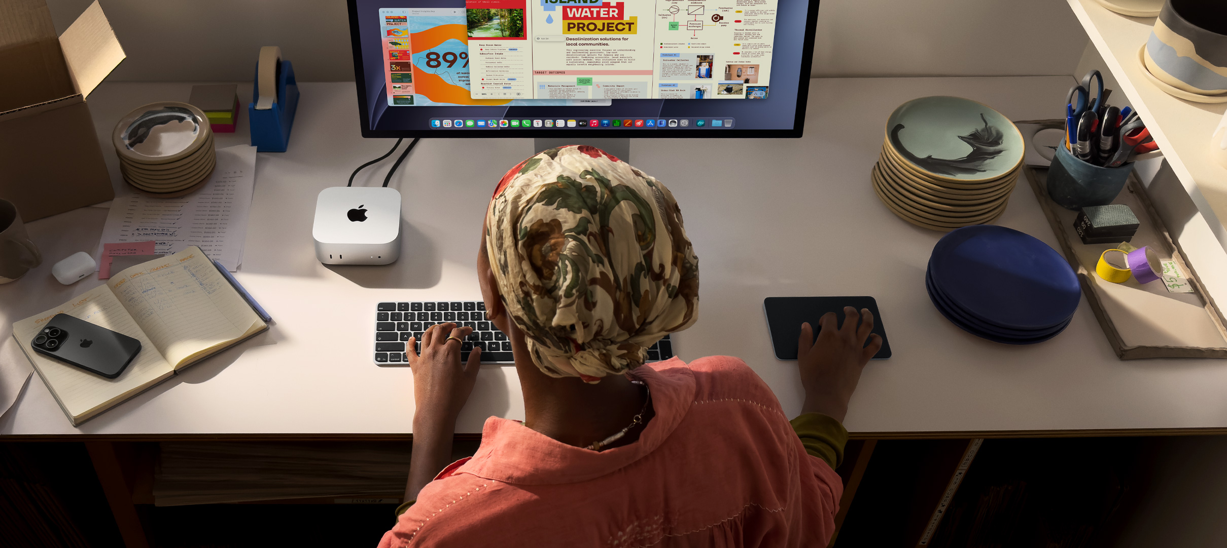 A person typing at a desk with a Mac mini, Studio Display connected, Magic Keyboard, Magic Trackpad, various items