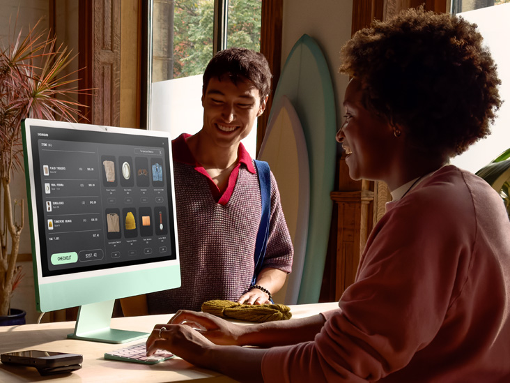 兩個人在一間光線充足的房間裡，其中一人在綠色 iMac M4 上查看訂單。